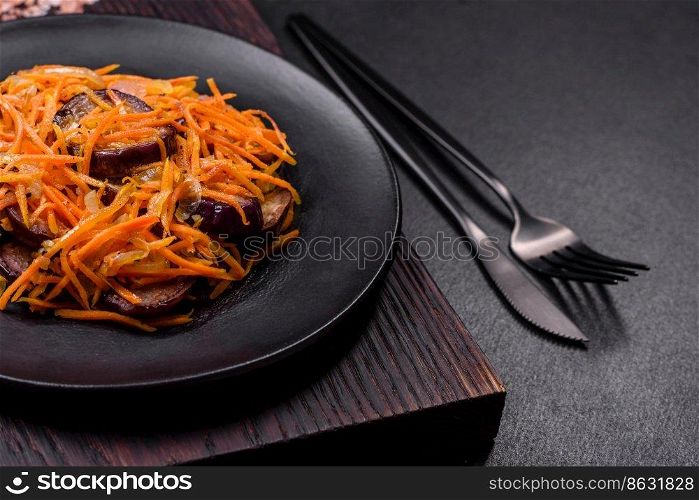 Korean salad with carrots and aubergine in a plate with garlic, black textured background. Korean salad with eggplant, carrots, garlic, spices and herbs on a dark concrete background
