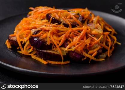 Korean salad with carrots and aubergine in a plate with garlic, black textured background. Korean salad with eggplant, carrots, garlic, spices and herbs on a dark concrete background