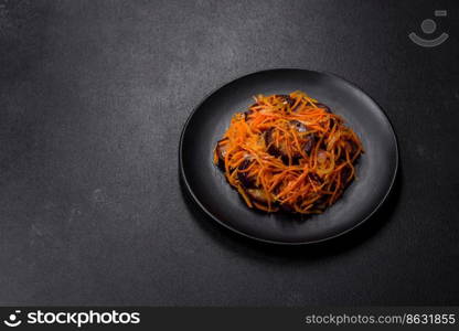 Korean salad with carrots and aubergine in a plate with garlic, black textured background. Korean salad with eggplant, carrots, garlic, spices and herbs on a dark concrete background