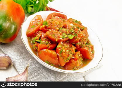 Korean style tomatoes with sweet and hot peppers, garlic and spices in a plate on a towel against white wooden board background