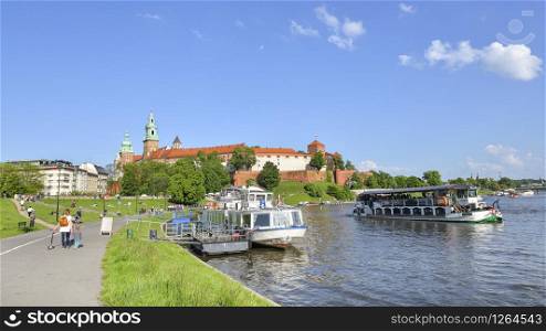 Krakow, Poland - May 20, 2019: Summer view on Wawel Castle, Vistula River, green park, bicycle lane and walking tourists. Summer view on Wawel Castle, Vistula River, spring park, bicycle lane and walking tourists