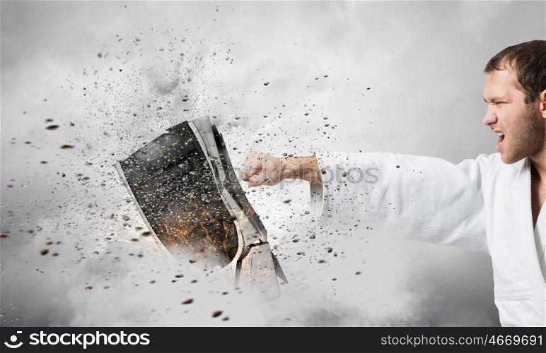 Krate man in action. Determined karate man in white breaking computer