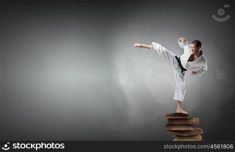 Krate man in action. Determined karate man on pile of old books