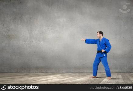 Krate man in action. Determined karate man practicing in empty room