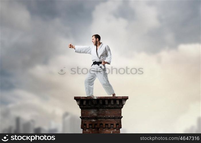 Krate man in action. Determined karate man training on building top