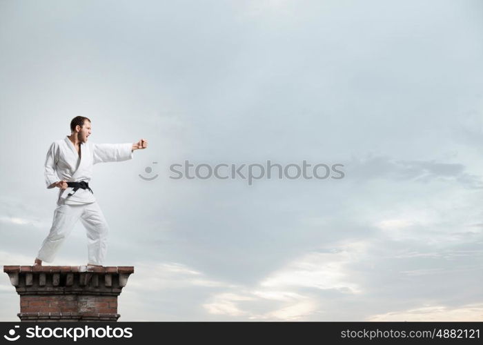 Krate man in action. Determined karate man training on building top