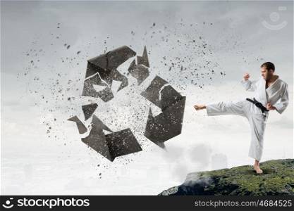 Krate man in action. Karate man in jump breaking recycle stone sign