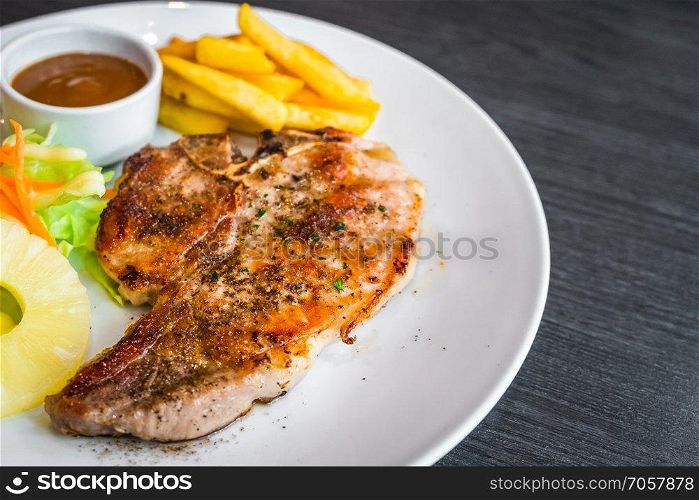 kurobuta pork chop with vegetable and french fries in white dish.