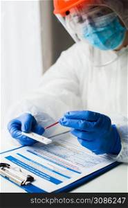 Lab technician medical scientist performing Coronavirus COVID-19 rapid diagnostic testing for antibodies, wearing personal protective equipment PPE, placing blood sample specimen on test using pipette