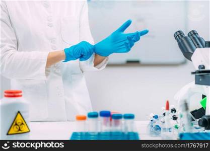 Lab technician putting on protective gloves. Laboratory safety equipment, hand protection.. Putting On Protective Gloves. Laboratory Safety Equipment.