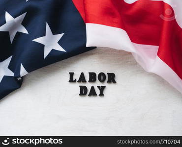 LABOR DAY. American flag and wooden letters of the alphabet on a white table. Close-up, top view. Bright photo with space for your inscriptions. Congratulations to relatives, friends and colleagues. Beautiful card with congratulations on Labor Day