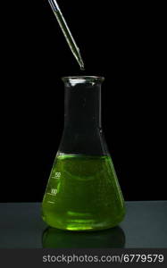 Laboratory beaker filled with green color liquid substances and laboratory pipette. Dark background