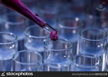 Laboratory glassware with pipette dropping red pink fluid into test tube