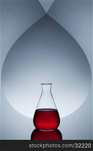 Laboratory glassware with red liquid on abstract background with reflection