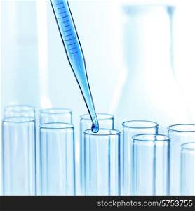 Laboratory pipette with drop of liquid over glass test tubes in a science research lab. Pipette with drop of liquid