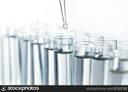 Laboratory pipette with drop of liquid over glass test tubes in a science research lab. Pipette with drop of liquid