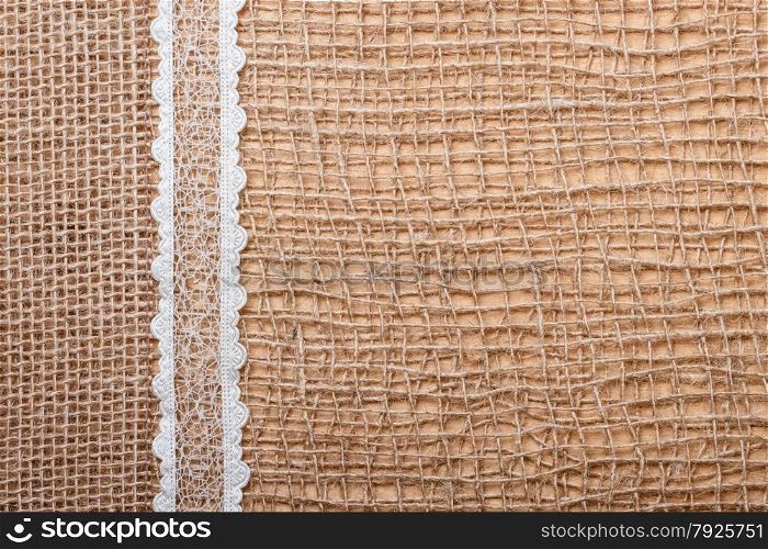 Lace and jute bagging ribbon on brown mesh material, natural burlap background