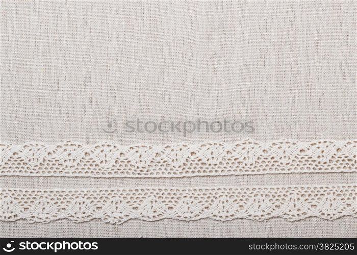 Lace ribbon on natural linen, bright cloth fabric background. Border frame