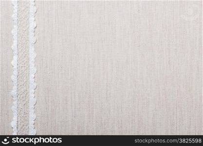 Lace ribbon on natural linen, bright cloth fabric background. Border frame