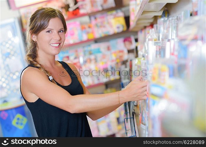 Lady arranging magazines on shelf in newsagents
