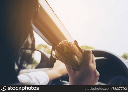 Lady driving car while eating hamburger