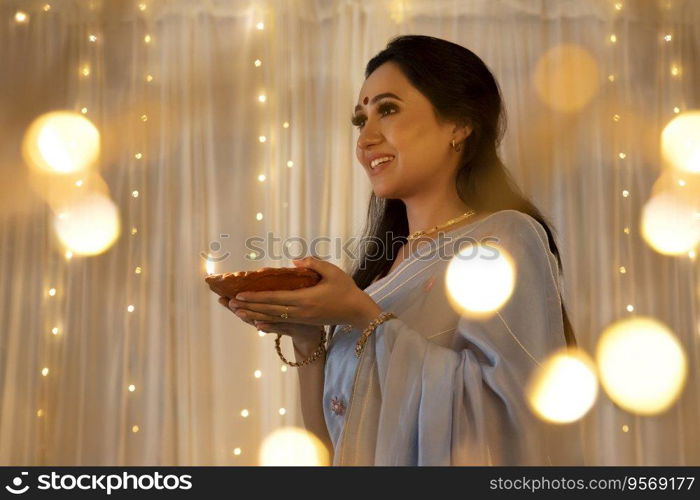 Lady in a beautiful saree smiling with a diya in her hands at home