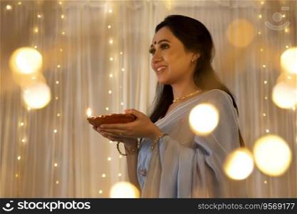 Lady in a beautiful saree smiling with a diya in her hands at home