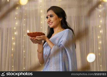 Lady in a saree smiling with a diya in her hand