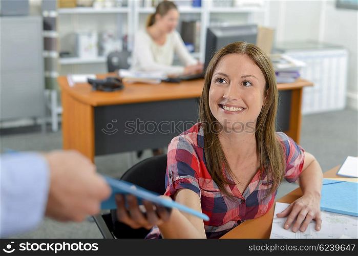 Lady in office being passed a file