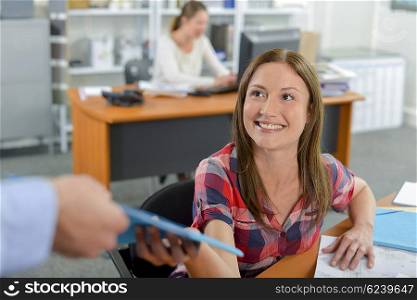 Lady in office being passed a file