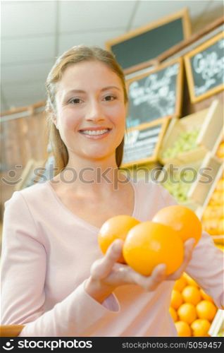 Lady in shop holding three oranges in her hand