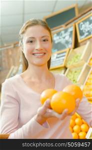 Lady in shop holding three oranges in her hand