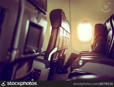 Lady is sitting in airplane looking out at shiny sun through window, vintage style photo