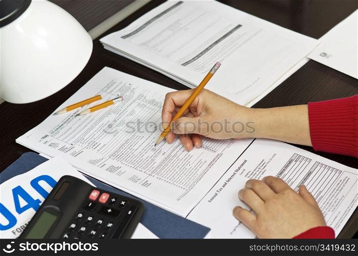Lady&rsquo;s hands working on tax forms with lamp, pencils, calculator and tax forms on desk top