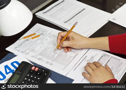 Lady&rsquo;s hands working on tax forms with lamp, pencils, calculator and tax forms on desk top