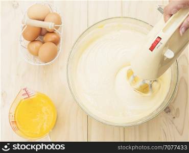 Lady's hand preparing cake using hand mixing machine with egg and butter