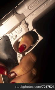 Lady spy detective with painted red nail varnish holding pistol gun at night