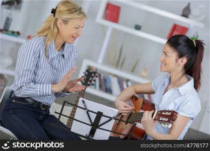 lady teaching young woman how to play guitar