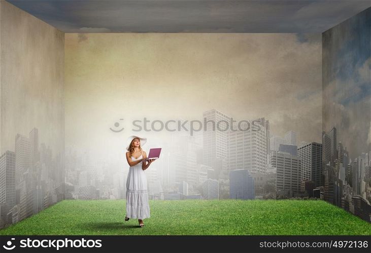 Lady using laptop. Young lady in white long dress and hat with laptop in hands