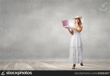 Lady using laptop. Young lady in white long dress and hat with laptop in hands