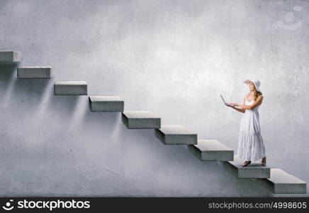 Lady using laptop. Young lady in white long dress and hat with laptop in hands