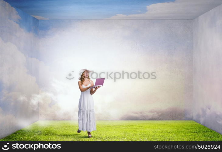 Lady using laptop. Young lady in white long dress and hat with laptop in hands