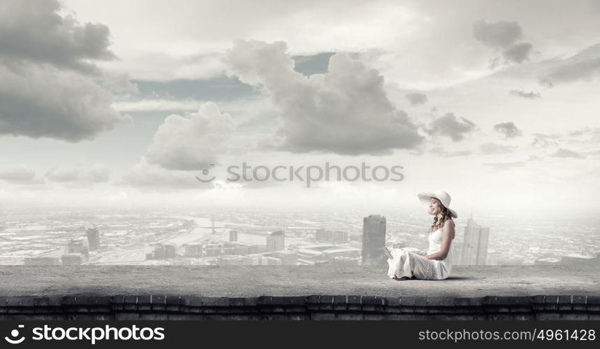 Lady using laptop. Young lady sitting on building roof with laptop on knees