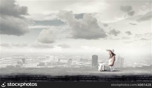 Lady using laptop. Young lady sitting on building roof with laptop on knees