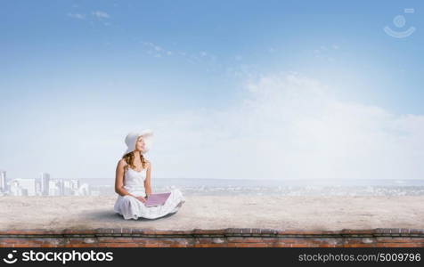 Lady using laptop. Young lady sitting on building roof with laptop on knees