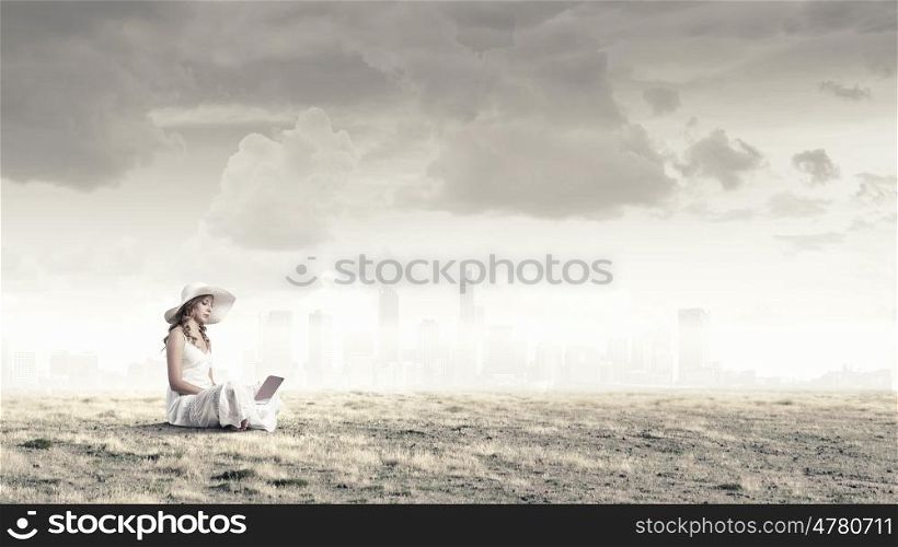 Lady using laptop. Young lady sitting on grass with laptop on knees