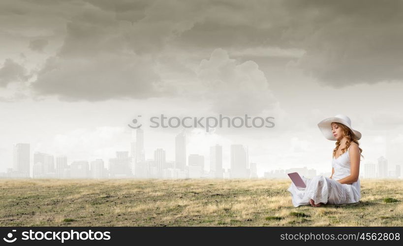 Lady using laptop. Young lady sitting on green grass with laptop on knees