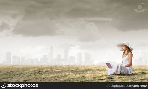 Lady using laptop. Young lady sitting on green grass with laptop on knees