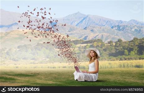 Lady using laptop. Young lady sitting on green grass with laptop on knees