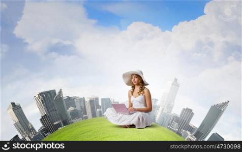 Lady using laptop. Young lady sitting on green grass with laptop on knees
